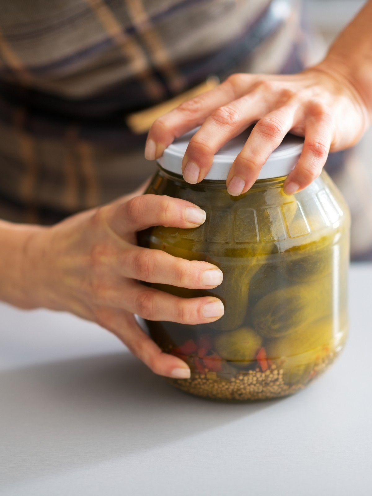 A person's hands struggling to twist the lid off a glass jar, illustrating the daily challenge of hand weakness.